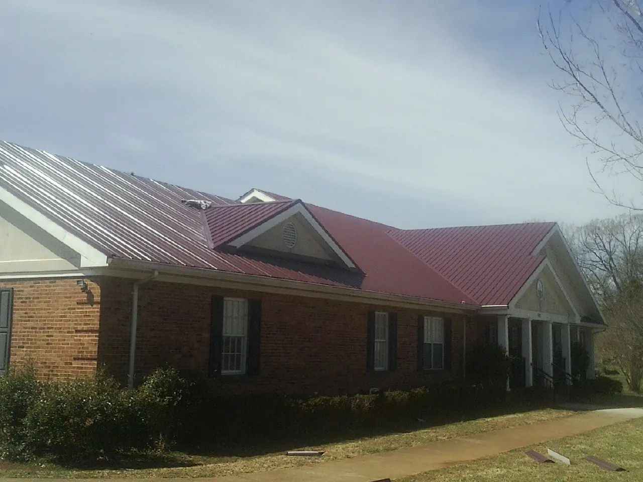 Red metal roof with gabled entries on a long brick building, from a Hail Damage Roof Repair job in Clyman