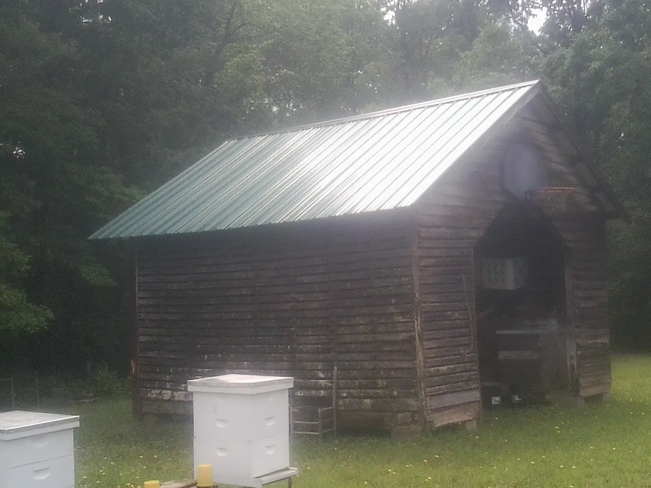 Green metal roof on a weathered barn beside stacked beehives in Clyman