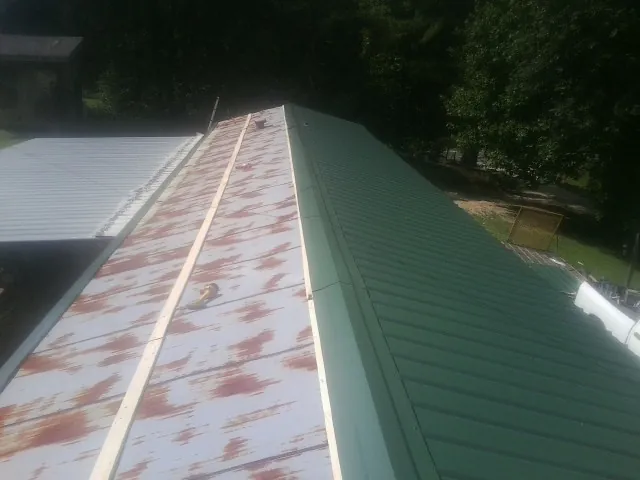 Old rusted panels beside newly installed green metal roofing — Wind Damage Roof Repair by Roofing Brothers in Clyman