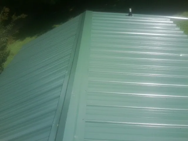 New green metal panels meeting at the ridge of a roof — Flat Roof Repair work by our crew in Clyman