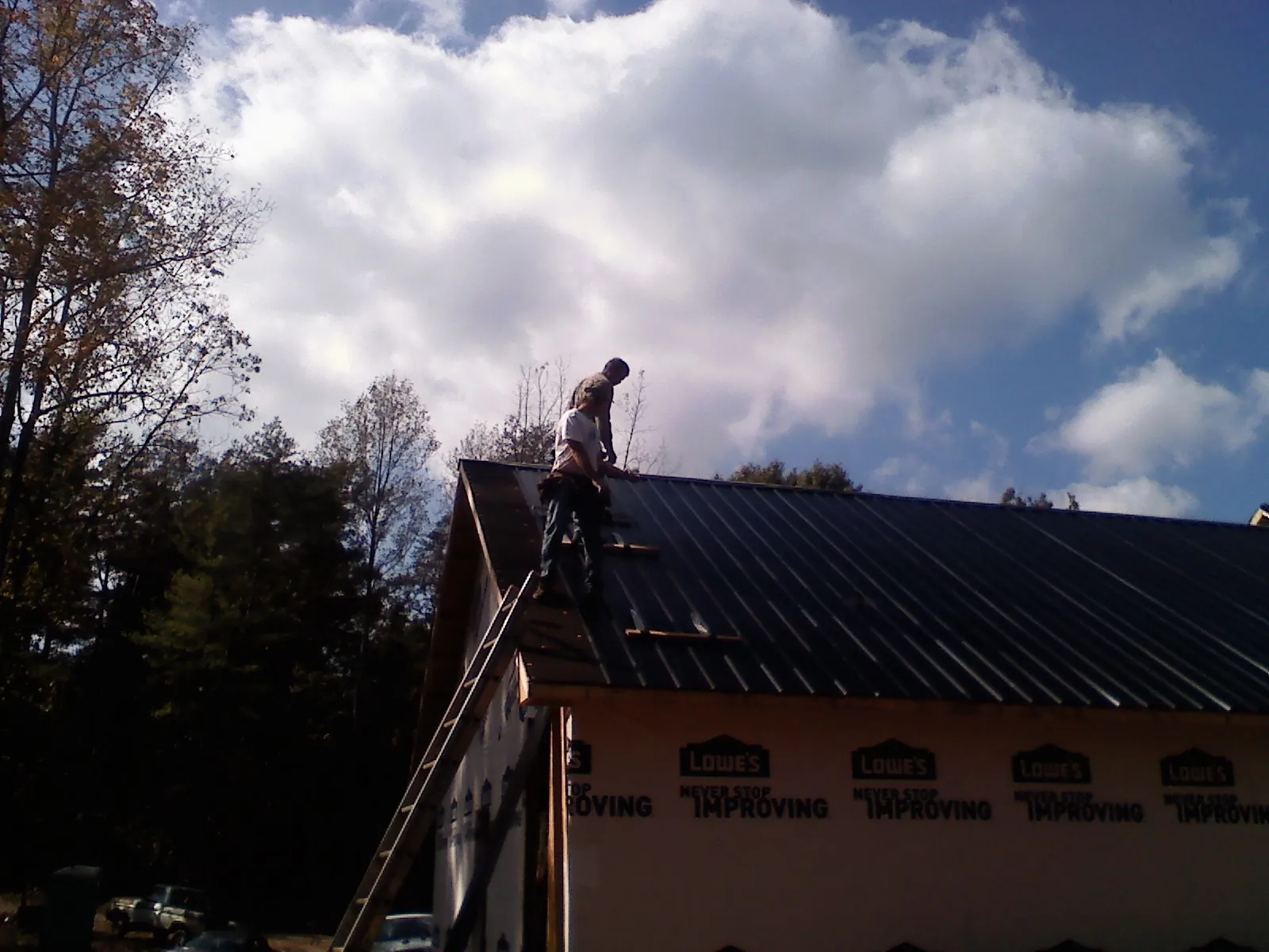 Roofer fastening dark metal panels high against a cloudy sky, from a Roof Inspection job in Clyman